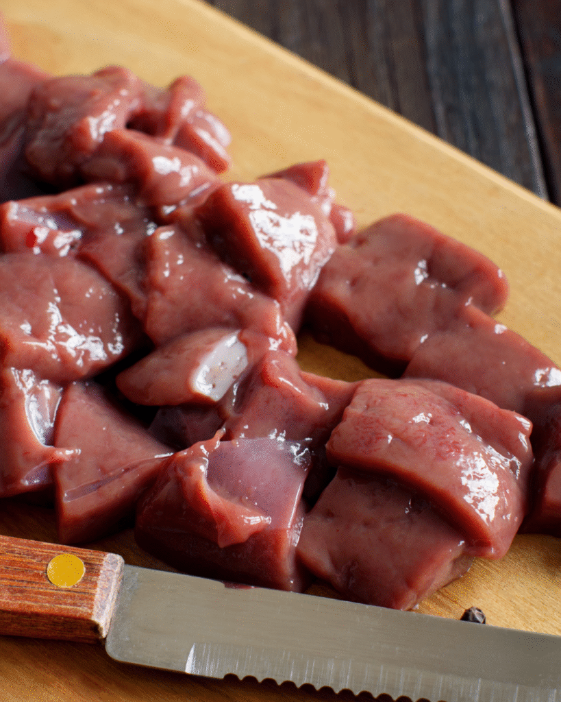 A fresh cut of beef liver placed on a wooden cutting board, rich in deep red color.